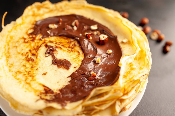 Homemade fresh crepes served with chocolate paste and hazelnuts on black stone background  - Foto, imagen