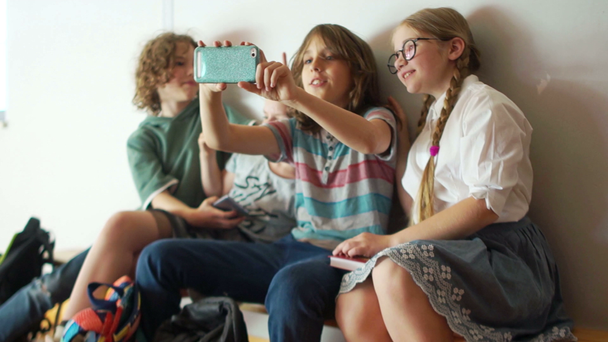 Teini-ikäiset valokuvattu älypuhelimet kamera koulun käytävällä tauon aikana. Salkkujen kanssa istuvat lapset penkillä, takaisin kouluun
 - Materiaali, video