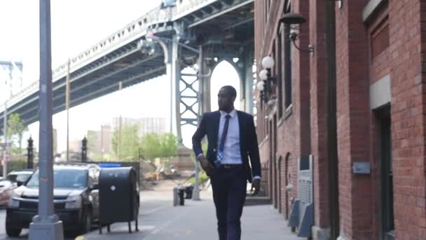 Young confident businessman walking at street on background of Manhattan Bridge, Brooklyn, New York City - Záběry, video
