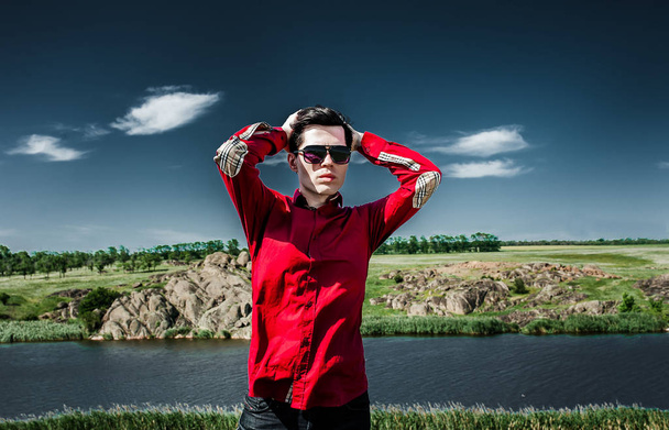 Młody stylowy człowiek w czerwonej koszulce stwarzające na zielonym tle krajobrazu - Zdjęcie, obraz