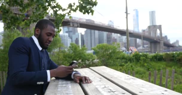 Young businessman in suit talking on smartpone while standing on background of Brooklyn Bridge  , New York City  - Materiał filmowy, wideo