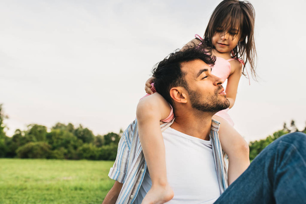 Image of happy cute little girl playing with father in the park during the sunset. Handsome dad is spending time with his little cheerful daughter outdoors. Fathers Day. Daddy and daughter shares love - Φωτογραφία, εικόνα