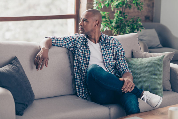 Profile side view photo of lovely charming attractive millennial sit divan peaceful gorgeous dressed denim jeans checked shirt apartment sneakers have thoughts - 写真・画像