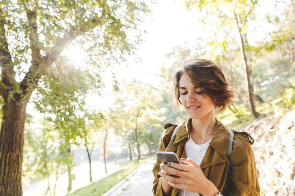 Young pretty woman walking outdoors in park in beautiful spring day using mobile phone. - 写真・画像