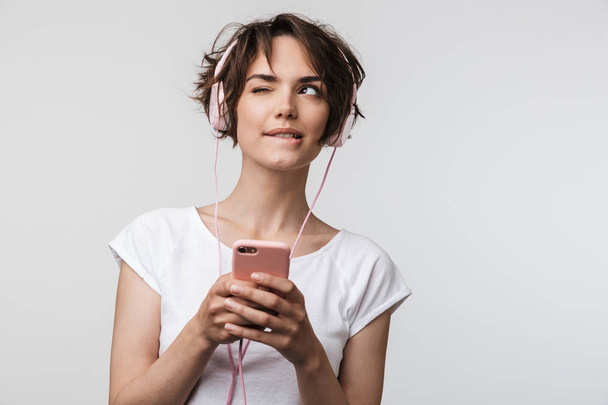 Image of young woman in basic t-shirt holding smartphone while l - Фото, зображення