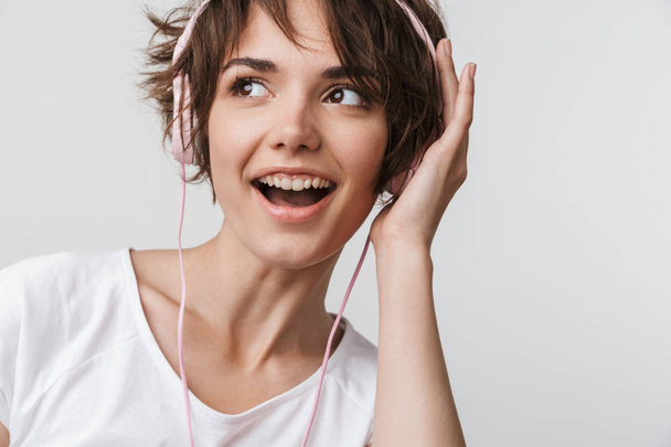 Pretty excited happy woman posing isolated over white wall background listening music with headphones. - Фото, изображение