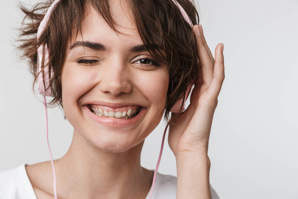 Pretty excited happy woman posing isolated over white wall background listening music with headphones. - Foto, Imagem