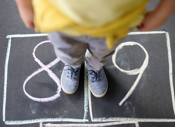 Closeup of little boy's legs and hopscotch drawn on asphalt. Child playing hopscotch game on playground outdoors on a sunny day. - Photo, Image