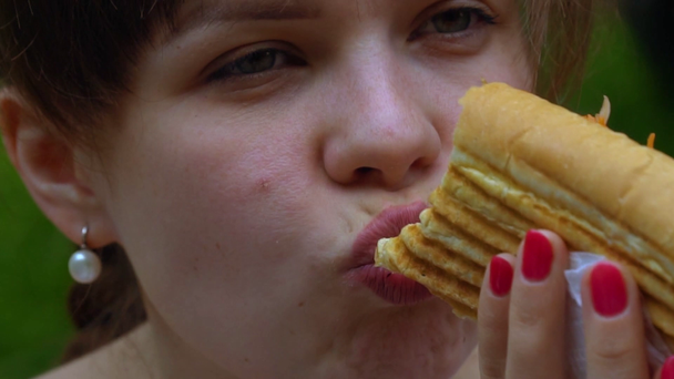 Κορίτσι που τρώει χοτ-ντογκ με ευχαρίστηση σε ένα πάρκο της πόλης. Αργή κίνηση - Πλάνα, βίντεο