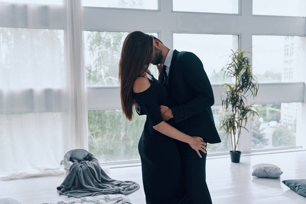 Beautiful young couple kissing and embracing while standing time in the bedroom - Valokuva, kuva