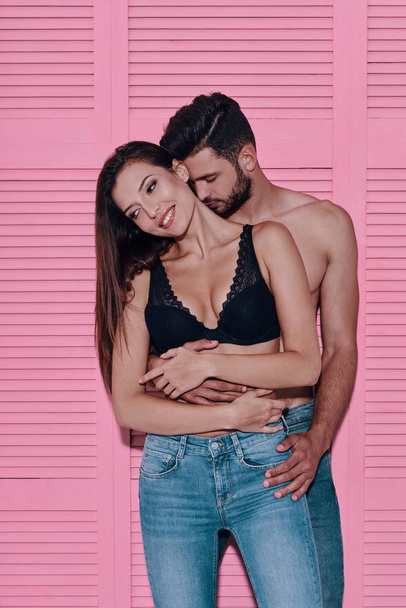 Beautiful young couple embracing and smiling while standing against pink background               - Fotó, kép