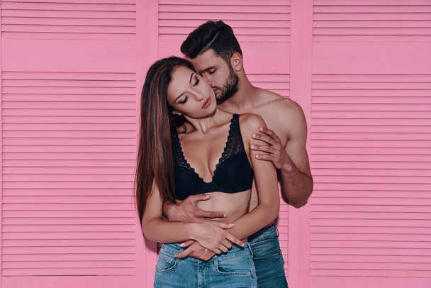 Beautiful young couple embracing while standing against pink background   - Fotografie, Obrázek