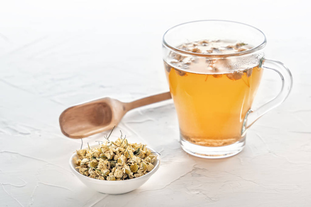 Травяной чай с фармацевтической ромашкой на белом столе
 - Фото, изображение