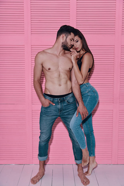 Full length of beautiful young couple embracing while standing against pink background - Fotó, kép