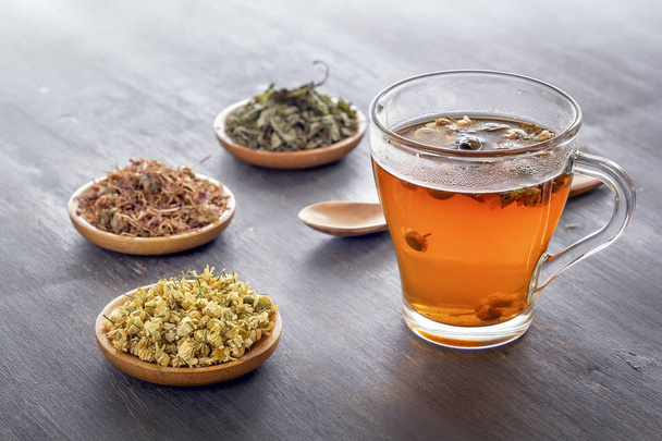 Chá de ervas com camomila farmacêutica, crisântemo seco e caçadores em uma mesa de madeira cinza
 - Foto, Imagem