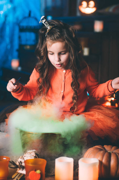 Egy kislány boszorkányjelmezben varázspálcával varázsitalt készít. - Fotó, kép