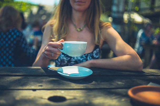 Молодая женщина пьет кофе в кафе на открытом воздухе летом
 - Фото, изображение