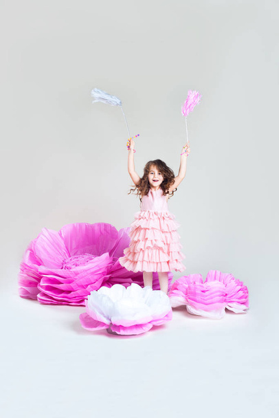 Pequeña niña saltando cerca de enormes flores de papel.  - Foto, imagen