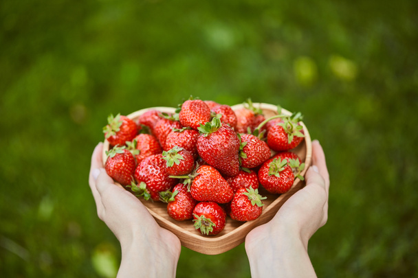 cropped view of woman holding heart shaped plate with raw strawberries - Foto, imagen