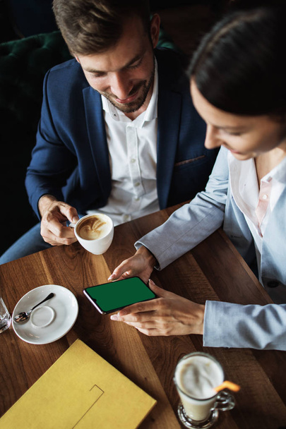 Mockup image of a business people holding smart mobile phone with blank green screen on vintage wooden table in modern cafe restaurant during meeting or lunch. - Valokuva, kuva