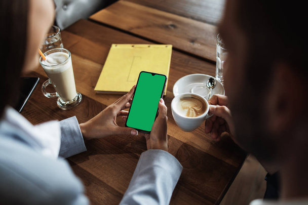 会議中や昼食中に現代のカフェレストランでヴィンテージ木製のテーブルの上に空白の緑の画面を持つビジネスの人々のモックアップイメージ. - 写真・画像