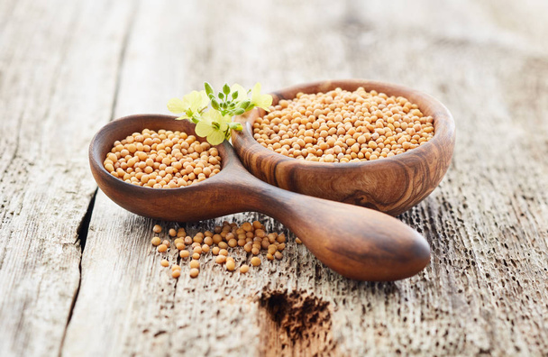 Mustard seeds with flowers on wooden background - Foto, afbeelding