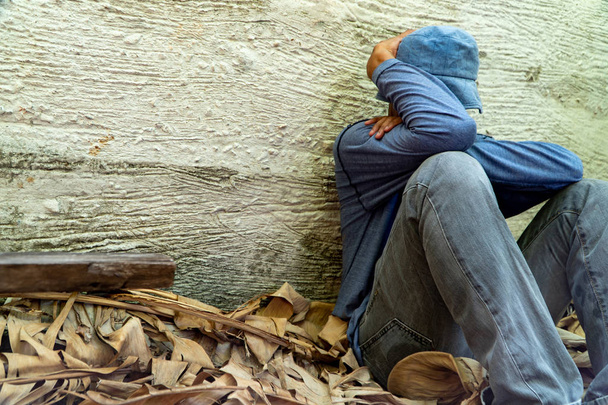Daklozen droeg een grijze hoed en een grijze lange mouwen shirt. Is slapen vanwege uitputting, met de terug leunend tegen de muur van Siemens - Foto, afbeelding