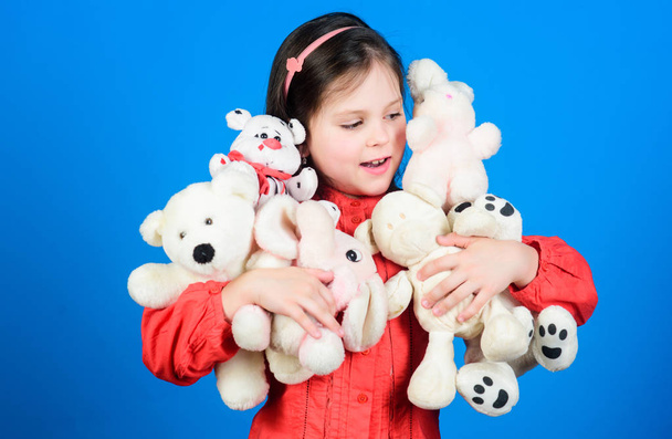 Small girl smiling face with toys. Happy childhood. Little girl play with soft toy teddy bear. Lot of toys in her hands. Childhood concept. Collecting toys hobby. Cherishing memories of childhood - Фото, изображение