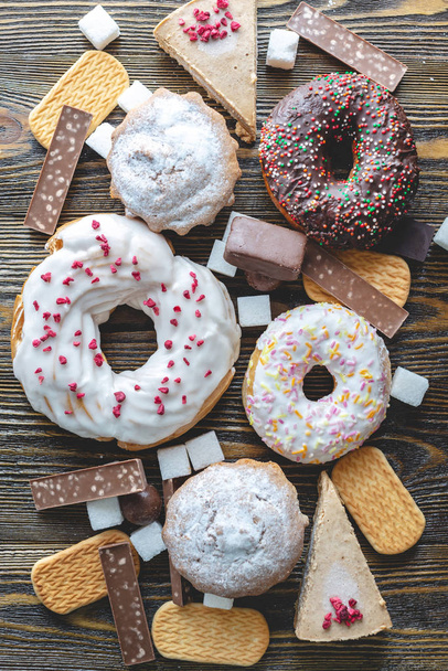 Schadelijk zoet voedsel op een donkere houten achtergrond. Donuts en muffins op de tafel stapel. Ongezond dieet en overgewicht - Foto, afbeelding