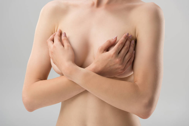 částečný pohled na sexy nahou dívku pokrývající prsa izolovaná na šedé - Fotografie, Obrázek