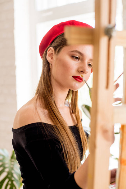 Attractive artist girl with long hair and red beret paints on an easel - Foto, Imagem
