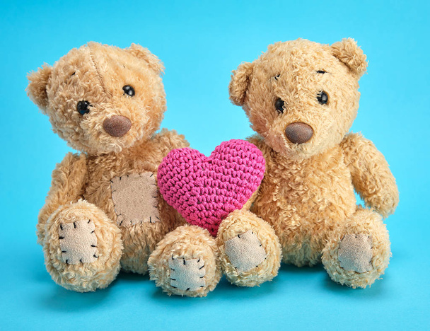twee bruine teddyberen houden een rood gebreid hart op een blauwe blauw - Foto, afbeelding