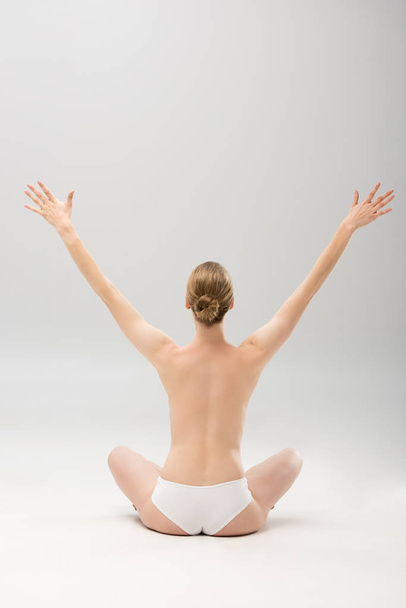 back view of young woman in panties sitting with hands up on grey - Photo, Image