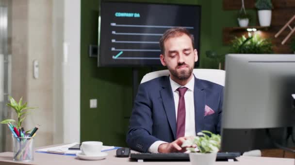 Office worker in suit types on computer keyboard, then looks at the time - Imágenes, Vídeo