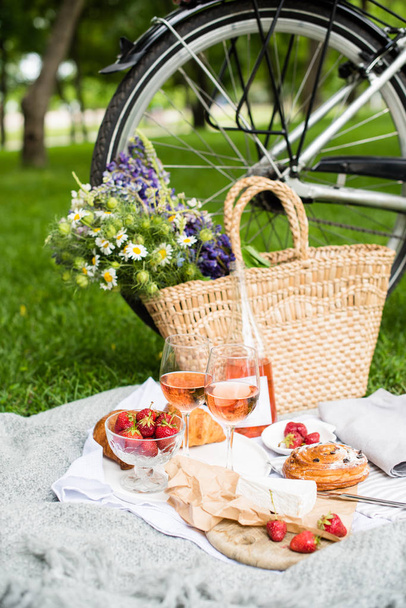 Прекрасный летний пикник с клубникой, сыром и розовым вином на лужайке в городском парке
 - Фото, изображение