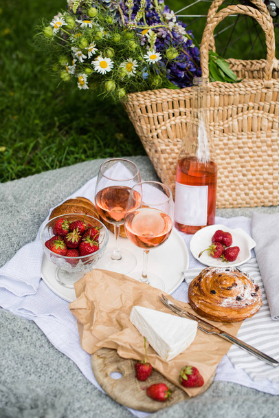 Beautiful summer picnic with strawberries, cheese and rose wine on the lawn in the city park - Фото, изображение