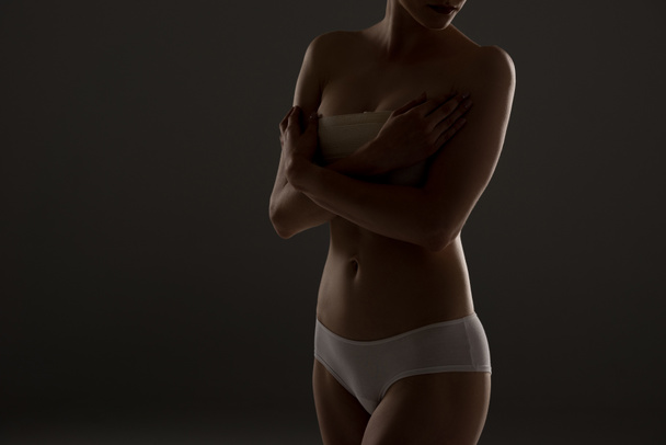 vista recortada de mujer en bragas con vendaje de pecho en la oscuridad
 - Foto, Imagen