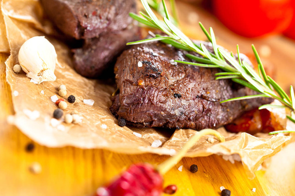 közeli kilátás ízletes grillezett szarvashús steak rozmaringos, fokhagyma, paradicsom és fűszerek az asztalra   - Fotó, kép