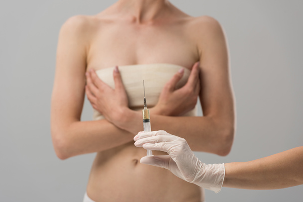 обрезанный вид пациента с повязкой на груди и врач в латексной перчатке, держащий шприц, изолированный на сером
 - Фото, изображение