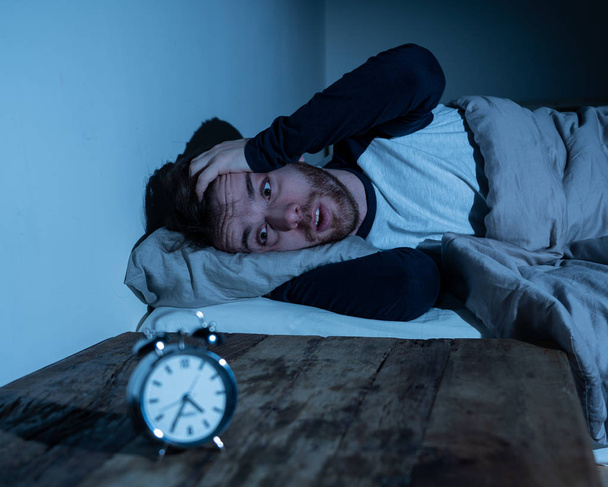 Schlaflosigkeit Stress und Schlafstörungen Konzept. schlaflose verzweifelte junge kaukasische Mann wach in der Nacht nicht in der Lage zu schlafen, fühlen sich frustriert und besorgt aussehen gestresst und besorgt am Wecker. - Foto, Bild