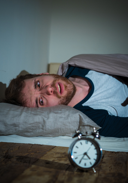 Mental health, Insomnia and sleeping disorders. Frustrated and hopeless sleepless man looking in distress at alarm clock awake at night not able to sleep suffering anxiety caused by stress at work. - Photo, Image