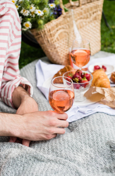 Mans hand holding glass of rose wine, summer picnic with cheese and wine - Фото, изображение