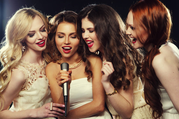 lifestyle, party and people concept - Four beautiful stylish girls singing karaoke at the club - Foto, Bild
