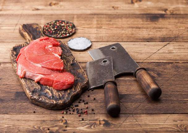 Fresh raw organic slice of braising steak fillet on chopping board with meat hatchets on wooden background. Salt and Pepper - Фото, зображення