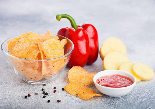 Glass bowl plate with potato crisps chips with paprika on light table background. Red paprika pepper with potatoes and sweet chilli sauce. - Foto, immagini