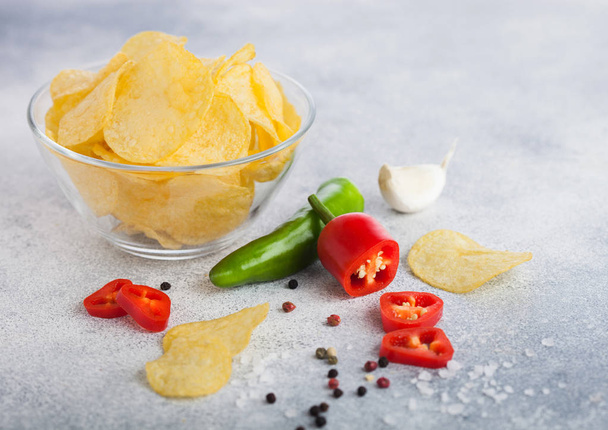 Glass bowl plate with potato crisps chips with onion flavour on light table background. Red and green chilli pepper with salt and garlic. - Foto, immagini