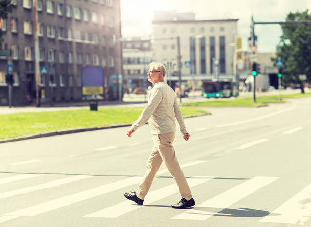 senior man walking along city crosswalk - Zdjęcie, obraz