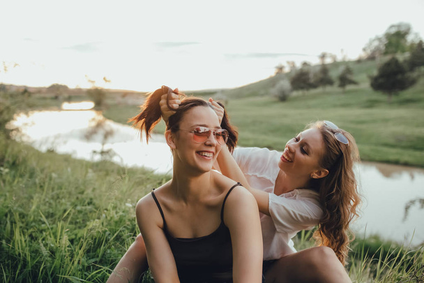 girls are having fun, they are down on the grass, at sunset, positive facial expression, outdoor, vacation and happiness concept - Photo, image