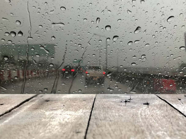 tableros de madera frente al parabrisas del coche con gotas de lluvia en el fondo borroso de la calle con el tráfico en la ciudad en el día lluvioso
 - Foto, imagen