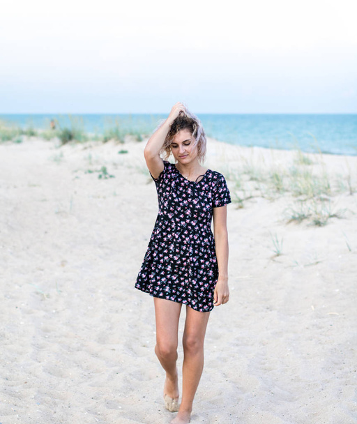 загорелая красивая молодая женщина в красивых платьях с цветами на пляже в облачную погоду
 - Фото, изображение